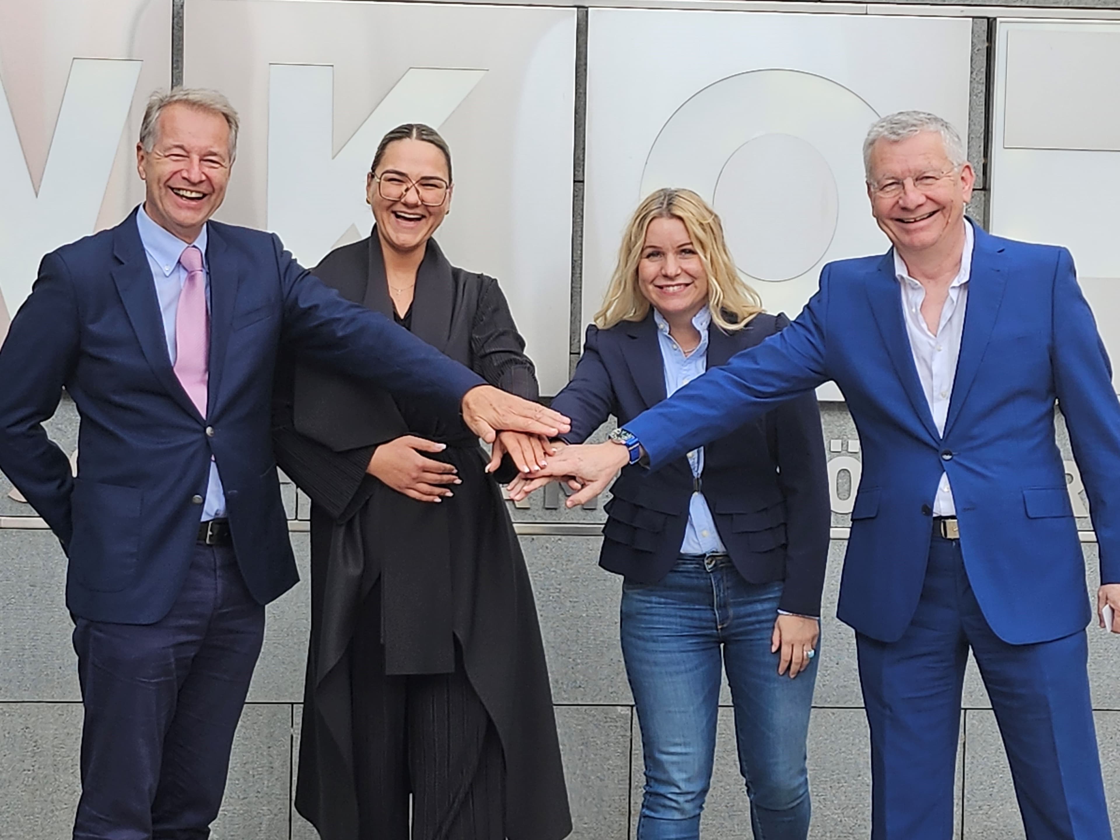 Kooperationsfoto vor dem WKO-Gebäude: vier Beteiligte legen ihre Hände als Zeichen der Zusammenarbeit zusammen.